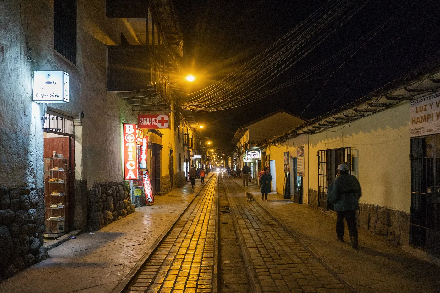 Calle comercial de Cusco de noche con boticas y tiendas